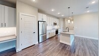 Located at 1980 Icon Way in Knoxville, Tennessee, this thoughtfully designed three-bedroom, three-bathroom home offers a clean, modern aesthetic throughout its single-floor layout. Warm hardwood-style flooring flows seamlessly through every room, complemented by neutral walls and crisp white trim that create a bright, cohesive atmosphere.

The kitchen serves as a central gathering point, featuring white shaker cabinetry extending to the ceiling, stainless steel appliances including a refrigerator, range, and built-in microwave, and a central island with pendant lighting and an undermount sink. The adjoining living area is filled with natural light from multiple windows and includes a ceiling fan for added comfort, with access to a private balcony overlooking a lush, wooded landscape.

Each bedroom is generously proportioned with natural light and dedicated closet space. The spacious primary bedroom connects to a walk-in closet and a well-appointed en suite bathroom featuring a double vanity with LED-lit mirrors, matte black fixtures, and a glass-enclosed tile shower. A secondary bathroom offers a tiled tub-shower combination with matte black hardware. Additional closets throughout provide ample storage, and a hallway connects all spaces with ease.