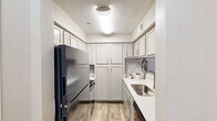 This thoughtfully designed one-bedroom, one-bathroom residence offers a comfortable and efficient layout across a single floor. The living room immediately impresses with its striking vaulted ceiling and an arched upper window that floods the space with natural light, creating an airy, open ambiance. Neutral-toned carpet and soft wall colors contribute to a calm, cohesive aesthetic throughout.

The galley-style kitchen is efficiently organized, featuring white shaker cabinetry that extends to the ceiling for generous storage, light wood-look flooring, a stainless steel sink, and stainless steel appliances including a full-size refrigerator and range. The adjacent dining area provides a cozy setting for meals, complemented by neutral carpet and warm, inviting tones.

The spacious primary bedroom is a restful retreat, offering plush carpeting, a ceiling fan with light fixture, and a window with views of the lush, tree-lined grounds outside. A dedicated closet provides ample storage.

The bathroom is finished with light wood-look flooring, an extended vanity with a white countertop, a large mirror, and built-in cabinetry. The hallway connects all spaces cleanly, and the surrounding outdoor environment features mature trees and well-maintained greenery, enhancing the overall sense of tranquility.