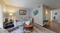 Located at 7049 Ulmerton Rd in Largo, Florida, this single-story residence offers a thoughtfully designed layout with a warm, neutral color palette carried throughout every room. The living room serves as a welcoming central gathering space, featuring wood-look flooring, a textured ceiling, and sliding glass doors with vertical blinds that invite natural light and offer views of the surrounding greenery. Adjacent to the living area, the dining room provides an elegant setting with ample space for a full dining set, a wall-mounted mirror that amplifies light, and continued access to outdoor views. The galley-style kitchen is efficiently arranged with white cabinetry, mosaic tile backsplash, light countertops, a stainless steel sink, and black appliances including a refrigerator, range, and dishwasher. Wood-look flooring ties the kitchen together with the main living spaces. The bedrooms are carpeted for comfort, each featuring windows with blinds that allow for natural light and outdoor views. The bathrooms are clean and functional, offering white vanity cabinetry, light countertops, wood-look flooring, and a shower-tub combination. The overall ambiance is calm and cohesive, with consistent finishes that make this a comfortable and move-in ready home.
