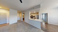 This single-floor residence offers a functional and comfortable layout designed for everyday living. The open-concept living area is anchored by plush wall-to-wall carpeting, neutral warm-toned walls, and a ceiling fan with integrated lighting. French doors allow natural light to flow in while providing access to the outdoors. The kitchen is positioned adjacent to the living space and features a peninsula with a single-basin sink and light stone countertops, white cabinetry, wood-look flooring, and a full suite of stainless steel appliances including a refrigerator, range, and over-the-range microwave. A dedicated dining area connects the two spaces seamlessly. The primary bedroom is generously sized, featuring soft carpeting, a ceiling fan, and a window for natural light. It connects to a bathroom outfitted with a stone-topped vanity, wood-look flooring, and access to a spacious walk-in closet. An additional bedroom offers similar finishes with its own ceiling fan, carpeted floor, window, and closet access. A separate laundry area with cabinetry is also present. Throughout the residence, consistent neutral tones and clean finishes create a cohesive, move-in-ready aesthetic.