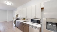 Located at 426 N Main St in Glen Ellyn, IL, this efficiently designed single-floor unit offers a well-considered layout comprising a living room, kitchen, bathroom, closet, and hallway. The living area is finished with light hardwood-style flooring and neutral white walls, creating a clean, airy atmosphere. A large window dressed with vertical blinds allows abundant natural light to fill the space, enhancing its open feel.

The kitchen is a standout feature, showcasing a contemporary two-tone design with dark wood-grain lower cabinetry contrasted by tall, light-toned upper cabinets that extend to the ceiling, maximizing storage. White quartz countertops, a classic subway tile backsplash, and stainless steel appliances — including a gas range, refrigerator, dishwasher, and built-in microwave — complete the modern, functional aesthetic.

The bathroom is thoughtfully equipped with accessibility in mind, featuring brushed nickel grab bars positioned near the toilet and along the wall, a white vanity with an integrated sink, and coordinating light hardwood-style flooring consistent with the rest of the unit.

Throughout, the space maintains a cohesive, minimalist design palette of whites and light neutrals, lending a fresh and functional character well-suited to everyday living.