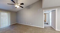 This single-floor, 2-bedroom, 1-bathroom home offers a practical and comfortable layout across a thoughtfully arranged floor plan. The living area features vaulted ceilings and a ceiling fan with light kit, creating an open and airy atmosphere. Neutral gray walls and plush wall-to-wall carpeting are consistent throughout the living and bedroom spaces, lending a cohesive and move-in-ready feel.

The primary bedroom is generously sized, featuring vaulted ceilings, a ceiling fan, and a large sliding glass door with vertical blinds that allows ample natural light. It also includes access to a dedicated walk-in closet equipped with wire shelving for organized storage. The second bedroom also offers a ceiling fan, carpeted flooring, and a window with vertical blinds.

The galley-style kitchen is efficiently designed with gray cabinetry, white countertops, and light wood-look flooring. It is equipped with black appliances, including a refrigerator, dishwasher, microwave, and electric range.

The bathroom features a tiled tub-shower combination, a vanity with a marble-look countertop and single sink, brushed nickel fixtures, and wood-look flooring. A hallway connects the main areas, and additional storage is available via a dedicated closet. The home also includes central HVAC with visible vents throughout.