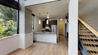 This contemporary two-story space showcases a thoughtfully designed open layout with clean lines and modern finishes throughout. The main level centers on an open-concept kitchen equipped with stainless steel appliances, including a refrigerator, microwave, and dishwasher. Dark espresso cabinetry contrasts elegantly with light quartz countertops, while pendant lighting above the kitchen island adds a refined touch. Large windows allow natural light to pour in, offering views of surrounding greenery and creating a bright, airy atmosphere.

Light hardwood flooring flows seamlessly throughout the main living areas, complementing the neutral white walls and contemporary aesthetic. A striking open staircase with a steel frame and wood treads serves as a design focal point, connecting the two floors while contributing to the industrial-modern character of the space. Built-in storage beneath the staircase makes practical use of the area.

The bathrooms are finished with tile flooring and feature clean, minimalist fixtures, including undermount sinks set in speckled stone vanity tops with dark cabinetry. The upper level, accessible via the open staircase, is visible from below through a metal railing, reinforcing the space's open, loft-like quality. Overall, the design balances modern sophistication with functional, well-organized living.