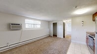 This single-floor residence at 115 Broadmeadow St in Marlborough, Massachusetts, offers a practical and well-organized layout across several distinct spaces. The interior is finished with neutral, light-toned walls throughout, creating a clean and consistent aesthetic. Carpeting covers the majority of the living and sleeping areas, while light-colored ceramic tile floors are found in the kitchen and bathroom.

The kitchen is efficiently designed, featuring warm-toned wood cabinetry, stainless steel appliances including a refrigerator, electric range, and microwave, along with a sink and ample counter space. A door provides direct exterior access from the kitchen area.

The living spaces are generously sized and naturally lit by multiple windows fitted with blinds. A standout feature is a curved bay window area in one of the rooms, which allows abundant natural light and adds architectural interest. Baseboard heating units line the walls throughout, and wall-unit air conditioners are present in several rooms for year-round climate control.

The bathroom is clean and functional, featuring tile flooring, a white vanity with a large mirror, and a grab bar. Closet space is available within the unit, including a reach-in closet with bifold doors. Textured ceilings are consistent throughout, contributing to the space's understated, practical character.