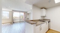 Located on the fourth floor at 1765 N Sycamore Ave in the heart of Hollywood, Los Angeles, this studio unit offers a well-planned single-level layout. The open-concept kitchen and living area form the core of the space, with light wood-tone flooring running seamlessly throughout, contributing to a bright and cohesive feel. The kitchen is designed in a galley style, featuring white cabinetry, granite-look countertops, a stainless steel refrigerator, a gas range with oven, a built-in microwave, and a dishwasher — providing a fully equipped cooking environment within a compact footprint. The living area is open and versatile, with neutral-toned walls, a textured ceiling, and a sliding glass door that invites natural light while offering access to an outdoor space and glimpses of the surrounding neighborhood, including a palm tree-lined view characteristic of the area. A dedicated closet provides generous storage with built-in shelving and a hanging rod, maximizing the functionality of the unit. The overall aesthetic is clean, modern, and move-in ready, making it a practical urban retreat in one of Los Angeles' most well-known neighborhoods.