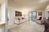 This single-floor residence offers a thoughtfully designed layout that balances comfort and functionality across its key living areas. The living room serves as the heart of the home, featuring plush wall-to-wall carpeting, a textured ceiling, and a sliding glass door that opens to an outdoor area, allowing natural light to fill the space. The open pass-through connects the living area seamlessly to the kitchen, which is outfitted with rich dark wood cabinetry, white countertops, stainless steel appliances including a range and over-the-range microwave, a built-in sink, and durable hardwood-style flooring. A dedicated dining area accommodates a round table and chairs beneath a decorative pendant light fixture, with easy access to the rest of the home. Two generously sized bedrooms each feature soft carpeting, ample natural light from large windows, and mirrored closet doors. The two full bathrooms are finished with tile flooring, dark wood vanities, light countertops, and well-lit mirrors. Throughout the residence, a neutral color palette and consistent finishes create a cohesive and inviting atmosphere suitable for everyday living.
