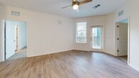This single-floor residence offers a clean, contemporary design throughout, with a thoughtful layout that balances open communal spaces with comfortable private quarters. The entryway opens into a bright, open-concept living area finished with warm wood-look luxury vinyl plank flooring and crisp white walls. A ceiling fan provides efficient climate control, while a glass-paneled exterior door and adjacent window invite natural light and outdoor views into the space.

The kitchen is a standout feature, showcasing gray shaker-style cabinetry, a white subway tile backsplash, and a full suite of stainless steel appliances including a refrigerator with ice maker, range, and microwave. A central island with pendant lighting overhead provides additional prep and gathering space, making it ideal for both everyday cooking and entertaining.

The bedrooms are carpeted for comfort and offer generous closet space, including a walk-in closet with wire shelving systems. The primary bathroom is particularly well-appointed, featuring a lengthy dual-sink vanity with gray cabinetry, a framed mirror, stylish sconce lighting, wood-look flooring, and a glass-enclosed shower. An additional bathroom provides further convenience. Throughout, the space maintains a cohesive, modern aesthetic with neutral tones and quality finishes.