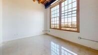 Located at 1614 Campbell Street in Oakland, CA, this studio unit offers a thoughtfully designed single-floor layout that combines industrial character with modern finishes. The main living area immediately draws attention with its striking exposed wooden beam ceiling, polished concrete floors, and white-painted brick walls that lend a raw, loft-like aesthetic. A large, multi-pane grid window framed in warm wood floods the space with natural light and provides an open view of the surrounding Oakland cityscape, creating an airy and bright atmosphere despite the compact footprint.

The galley-style kitchen is efficiently laid out along one wall and is well-equipped with stainless steel appliances, including a full-sized refrigerator, gas range, and built-in microwave. Dark lower cabinetry paired with white upper cabinets and a dark stone countertop offer a sleek, contemporary contrast. The polished flooring continues throughout, enhancing the sense of continuity and cleanliness.

The bathroom features a clean, functional design with a white vanity topped with a dark countertop, a wall-mounted mirror, and accessibility-friendly grab bars. Warm-toned flooring adds a subtle contrast to the neutral walls. A ceiling-mounted heater unit in the main room and visible utility elements reinforce the space's industrial character, making this studio a distinctive and practical urban retreat.