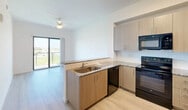 Located along S Dixie Highway in Homestead, FL, this one-bedroom, one-bathroom unit offers a well-designed single-floor layout with a clean, modern aesthetic. The open-concept kitchen and living area is the heart of the unit, featuring light wood-look flooring, a ceiling fan, and sliding glass doors that lead to a private balcony with scenic outdoor views of the surrounding landscape. The kitchen is equipped with black appliances including an electric range, built-in microwave, and refrigerator, complemented by light wood cabinetry, white subway tile backsplash, and granite countertops with an integrated sink. The bedroom is a bright and comfortable space with light-toned hardwood-style flooring, crisp white walls, and a large window framing views of palm trees and greenery. Three closets provide ample storage throughout the unit. The bathroom features a granite-topped vanity with wood cabinetry, large-format light tile flooring, and a full soaking tub with a tiled surround and curved curtain rod. Additional spaces include a laundry area, utility room, and hallway, rounding out a thoughtfully organized and functional floor plan with a fresh, contemporary feel.