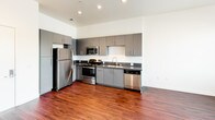 Located at 3050 Mission Inn Ave in Riverside, California, this single-floor unit offers a thoughtfully designed layout with modern finishes throughout. The kitchen is a standout feature, showcasing sleek gray flat-front cabinetry extending to the ceiling for ample storage, dark countertops, and a full suite of stainless steel appliances including a refrigerator, electric range, over-the-range microwave, and dishwasher. Recessed lighting illuminates the space, while rich hardwood-style flooring ties the kitchen and open living area together seamlessly. The bedroom is generously proportioned, featuring soft carpeting, crisp white walls, and a large window that invites abundant natural light and views of the surrounding neighborhood. The vaulted ceiling adds a sense of openness and volume to the room. The bathroom is clean and functional, finished with hardwood-style flooring consistent with the rest of the unit, a gray vanity with a built-in sink, a large mirror, and a full tub-shower combination with white tile surround. The overall aesthetic of the unit is contemporary and understated, with a neutral palette that provides a versatile backdrop for a variety of interior styles.
