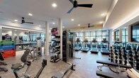 Located at 5840 Farrington Rd in Chapel Hill, NC, this single-level fitness center is a comprehensively outfitted facility designed to support a wide range of workout routines. The space is organized into distinct functional zones while maintaining an open, cohesive layout throughout.

The cardio area features a row of modern treadmills and elliptical machines positioned along a wall of floor-to-ceiling steel-framed windows, offering views of an outdoor terrace and surrounding tree line. Natural light floods this section of the facility, creating an energizing environment for cardio training. Large mirrors along adjacent walls visually expand the space and allow users to monitor their form.

The strength and functional training zone is well-stocked with Precor cable machines, a leg press, free weights, kettlebells, medicine balls, resistance bands, and Plyosoft plyo boxes. Equipment racks are neatly organized, and structural columns divide the space without interrupting the overall flow.

A separate studio room, accessible through sleek black-framed glass doors, features hardwood flooring and is suited for group classes, stretching, or individual training sessions. Digital displays and mounted screens are integrated throughout.

Recessed lighting, ceiling fans, and durable flooring complete the polished, modern aesthetic of this well-appointed fitness facility.