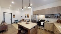 This well-designed single-floor residence blends modern aesthetics with warm, inviting elements throughout its thoughtfully arranged layout. The open-concept kitchen and living area serves as the heart of the home, where a striking wood-paneled island with light stone countertops anchors the space beneath a trio of industrial-style pendant lights. The kitchen is fully equipped with stainless steel appliances, including a French door refrigerator and electric range, complemented by light wood cabinetry, a textured tile backsplash, stone countertops, a deep undermount sink with a matte black faucet, and rustic open shelving. Wood-look flooring flows seamlessly throughout, enhancing the cohesive, contemporary feel. The living area offers a welcoming atmosphere with clean white walls, recessed lighting, and a cozy seating arrangement. Two bedrooms provide comfortable private retreats, each with soft neutral tones and natural light from well-placed windows. The bathroom features a spacious layout with dark wood vanity, stone countertops, tile flooring, and a walk-in shower with decorative tile accents. The entry includes a bold black-framed door and direct access to a secondary exterior door, adding both style and convenience to this smartly designed residence.