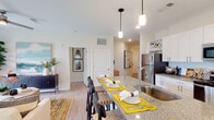 Located at 5214 Browning Ln in Leland, NC, this single-story home offers a thoughtfully designed layout with modern finishes and a bright, welcoming atmosphere throughout. The open-concept kitchen is a standout feature, showcasing white shaker cabinetry, granite countertops, a subway tile backsplash, stainless steel appliances, and a large center island with bar seating illuminated by pendant lighting — ideal for both everyday living and entertaining. Light wood-tone flooring flows seamlessly throughout the home, enhancing the sense of continuity and space. The living room is filled with natural light from sliding glass doors that open to an outdoor view, creating an airy and comfortable gathering space. The bedroom features a ceiling fan, a generous window with exterior views, and ample room for a large bed and furnishings. A spacious walk-in closet with wire shelving and hanging rods provides excellent storage. The bathroom is clean and functional, with a white vanity and wood-look flooring. A dedicated laundry area houses a full-size washer and dryer with open shelving above for added convenience. Together, these features create a well-rounded, move-in-ready home with a cohesive and comfortable design.