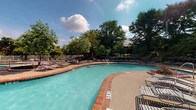 Located at 5407 Edwards Plantation Dr in Columbus, Ohio, this single-level outdoor amenity space centers around a generously sized freeform swimming pool with clear, turquoise water. The pool features a classic brick-edged coping that adds a timeless, well-maintained aesthetic to the area. Depth markers are clearly visible along the pool's perimeter, reflecting a commitment to safety and functionality.

Surrounding the pool is a spacious concrete sundeck designed to accommodate a wide array of lounge chairs and seating, offering ample room for relaxation and recreation. The deck transitions seamlessly into a secondary patio area shaded by mature, full-canopy trees that frame the space beautifully and provide natural relief from the sun.

The landscape is lush and verdant, with well-established trees and plantings creating a private, resort-like atmosphere. A perimeter fence encloses the pool area, ensuring security while maintaining an open, airy feel. The overall ambiance is inviting and recreational, well-suited for outdoor leisure throughout the warmer months. The combination of the sparkling pool, broad sundeck, and richly wooded backdrop makes this community amenity a standout outdoor gathering destination in the Columbus area.
