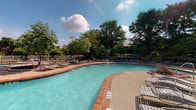Located at 5407 Edwards Plantation Dr in Columbus, Ohio, this single-level outdoor amenity space centers around a generously sized freeform swimming pool with clear, turquoise water. The pool features a classic brick-edged coping that adds a timeless, well-maintained aesthetic to the area. Depth markers are clearly visible along the pool's perimeter, reflecting a commitment to safety and functionality.

Surrounding the pool is a spacious concrete sundeck designed to accommodate a wide array of lounge chairs and seating, offering ample room for relaxation and recreation. The deck transitions seamlessly into a secondary patio area shaded by mature, full-canopy trees that frame the space beautifully and provide natural relief from the sun.

The landscape is lush and verdant, with well-established trees and plantings creating a private, resort-like atmosphere. A perimeter fence encloses the pool area, ensuring security while maintaining an open, airy feel. The overall ambiance is inviting and recreational, well-suited for outdoor leisure throughout the warmer months. The combination of the sparkling pool, broad sundeck, and richly wooded backdrop makes this community amenity a standout outdoor gathering destination in the Columbus area.