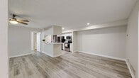 This single-floor residence offers a clean, modern aesthetic defined by a neutral color palette, light wood-look flooring, and a textured ceiling carried consistently throughout the space. The open-concept living and kitchen area serves as the heart of the home, where a peninsula with a white countertop separates the two zones while maintaining a sense of openness. The kitchen is equipped with stainless steel appliances — including a range, microwave, and refrigerator — set against white cabinetry and recessed lighting overhead. The living area is generously sized and connects directly to a private outdoor space via sliding glass doors framed by vertical blinds and topped with a ceiling fan for added comfort. The bedrooms are bright and well-proportioned, each featuring ceiling fans with light fixtures and windows that bring in natural light. The primary bedroom benefits from dual windows and direct access to a walk-in closet. Both bathrooms are finished in white, featuring vanities with under-cabinet storage, large mirrors, and modern light fixtures. The overall layout is efficient and thoughtfully designed, offering a cohesive and move-in-ready living environment that balances functionality with contemporary style.