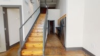 This two-story space showcases a compelling industrial aesthetic rooted in its original architectural bones. The main level features polished concrete floors that carry a warm, earthy tone throughout, complementing the prominent exposed brick walls that serve as striking focal points in multiple rooms. Soaring ceilings amplify the sense of openness, while large multi-pane windows allow natural light to flood the interior, casting dramatic shadow patterns across the floors.

The kitchen is efficiently designed with light wood cabinetry, dark granite countertops, and a full suite of stainless steel appliances, including a refrigerator, range, microwave, and dishwasher. It connects seamlessly to adjacent living areas defined by their raw brick backdrops and concrete ceiling details.

A staircase with warm-toned natural wood treads and a sleek metal railing leads to the upper level, where the loft area features hardwood flooring and a sloped concrete ceiling that adds architectural interest. A ceiling fan services one of the upper rooms, which also benefits from an exposed brick accent wall and a glass-block window.

Two bathrooms are finished with large-format dark tile flooring, full tub-shower combinations, wood cabinetry, and clean, understated fixtures. The overall ambiance is distinctly urban and industrial, balanced by modern updates throughout.
