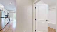 This well-designed single-floor unit offers a thoughtfully arranged layout that maximizes its intimate footprint. Light-toned hardwood-style flooring runs consistently throughout, creating a cohesive and clean aesthetic that ties the space together.

The kitchen serves as a standout feature, showcasing crisp white shaker cabinetry, quartz countertops, and a striking dark subway tile backsplash. Stainless steel appliances — including a refrigerator, range, dishwasher, and over-the-range microwave — provide a modern, functional cooking environment. A large sliding glass door adjacent to the kitchen floods the area with natural light and opens to a private balcony overlooking lush, mature greenery.

The open living area is bright and airy, benefiting from recessed lighting and additional natural light from the balcony access. Neutral warm-white walls complement the light flooring and contribute to the overall sense of openness.

The full bathroom is finished to a high standard, featuring white shaker-style vanity cabinetry, a quartz countertop with an undermount sink, brushed nickel fixtures, a large mirror, and a full tub-shower combination — all set atop matching hardwood-style flooring.

A hallway with a paneled interior door connects the rooms, offering practical separation and privacy. The unit presents a clean, move-in-ready condition with a modern, neutral palette throughout.