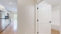 This well-designed single-floor unit offers a thoughtfully arranged layout that maximizes its intimate footprint. Light-toned hardwood-style flooring runs consistently throughout, creating a cohesive and clean aesthetic that ties the space together.

The kitchen serves as a standout feature, showcasing crisp white shaker cabinetry, quartz countertops, and a striking dark subway tile backsplash. Stainless steel appliances — including a refrigerator, range, dishwasher, and over-the-range microwave — provide a modern, functional cooking environment. A large sliding glass door adjacent to the kitchen floods the area with natural light and opens to a private balcony overlooking lush, mature greenery.

The open living area is bright and airy, benefiting from recessed lighting and additional natural light from the balcony access. Neutral warm-white walls complement the light flooring and contribute to the overall sense of openness.

The full bathroom is finished to a high standard, featuring white shaker-style vanity cabinetry, a quartz countertop with an undermount sink, brushed nickel fixtures, a large mirror, and a full tub-shower combination — all set atop matching hardwood-style flooring.

A hallway with a paneled interior door connects the rooms, offering practical separation and privacy. The unit presents a clean, move-in-ready condition with a modern, neutral palette throughout.