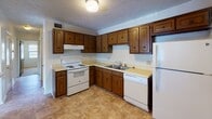 This single-story residence in Radford, Virginia offers a straightforward, functional layout well-suited for everyday living. The kitchen is outfitted with rich, dark wood cabinetry providing ample upper and lower storage, light-toned countertops, and a double-basin sink. White appliances, including an electric range, dishwasher, and refrigerator, are all included. Tile-style flooring runs throughout the kitchen, adding durability to a practical space. A pass-through window connects the kitchen to the adjacent living and dining area, which features neutral carpet, a textured ceiling, and a pendant light fixture. The living space is generously proportioned, providing flexibility for various furniture arrangements. Carpeted bedrooms offer a quieter, softer feel, with windows that bring in natural light. The bathroom includes a wide vanity with dark wood cabinetry, a large mirror, light countertop, and a tub-shower combination. Throughout the unit, neutral wall tones and textured ceilings create a consistent, understated aesthetic. Louvered closet doors add a classic touch, and interior layout is efficiently organized for comfortable, single-floor living.