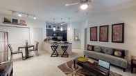 This single-floor residence offers a thoughtfully designed open-concept layout connecting the living, dining, and kitchen areas into one cohesive space. The kitchen is a standout feature, equipped with rich dark cabinetry, granite countertops, black appliances including a range, microwave, and refrigerator, and wood-style flooring. A wraparound peninsula with pendant lighting above and bar seating provides both additional prep space and a casual dining option.

The living area is carpeted and filled with natural light from large windows dressed with blinds and decorative curtains. A ceiling fan with integrated lighting anchors the room, while track lighting adds supplemental illumination throughout the open space.

Both bedrooms are generously sized with plush carpet, ceiling fans, and large windows. One bedroom includes a walk-in closet with built-in shelving, while the other offers ample storage as well. Each bathroom features a dark wood vanity with granite-style countertops and a full tub-shower combination with white tile surround and wood-style flooring, providing a clean, functional finish throughout.