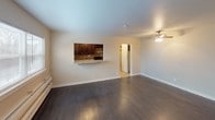 This studio unit at The Isles offers a well-organized, single-floor layout designed to maximize functionality within a compact footprint. The open living area features rich, dark hardwood flooring that runs throughout, creating a warm and cohesive aesthetic. A ceiling fan provides comfortable airflow, while a window along one wall allows natural light to brighten the space. A baseboard heating unit ensures year-round comfort.

The kitchen is accessible via a convenient pass-through window with a granite-style countertop ledge, ideal for casual dining or entertaining. Inside, the kitchen is thoughtfully appointed with dark espresso cabinetry, a mosaic tile backsplash in warm earth tones, granite-look countertops, a stainless steel double-basin sink with a modern pull-down faucet, and a black electric range. Upper and lower cabinetry provide ample storage.

The bathroom features a full tub and shower combination with a clean white surround, stainless steel grab bars for added safety and accessibility, and dark espresso wall-mounted cabinetry for additional storage. The neutral, light-toned walls throughout the unit create a bright and versatile backdrop, making the space easy to personalize and furnish.