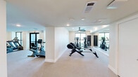 Located at 1601 Scottsdale Lane in Austin, TX, this single-floor fitness facility offers a comprehensive workout environment across two dedicated exercise rooms. The space is designed with a clean, modern aesthetic, featuring neutral-toned carpet flooring, crisp white walls, and recessed lighting throughout, creating a bright and energizing atmosphere.

The first exercise room is generously sized and serves as the primary strength and cardio zone. It is outfitted with a multi-station cable machine, a weight bench, a full dumbbell rack, and ample open floor space. Floor-to-ceiling mirrors span entire walls, visually expanding the room and allowing for proper form checks during workouts. Ceiling fans provide airflow and comfort during intense sessions.

The second exercise room is dedicated to cardio equipment, housing rowing machines, treadmills, ellipticals, and stationary bikes. Large windows and a glass sliding door flood this area with natural light and offer views of the surrounding outdoor landscape, enhancing the workout experience. A wall-mounted television adds entertainment options for cardio sessions.

Additional features include built-in shelving for storage, modern ventilation systems, and a layout that encourages smooth circulation between zones. The facility is thoughtfully designed to support a wide range of fitness activities in a comfortable, well-maintained environment.