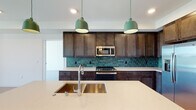 This thoughtfully designed single-floor residence combines contemporary finishes with functional living spaces. The kitchen serves as the heart of the home, showcasing rich dark wood cabinetry, a striking teal subway tile backsplash, and a full suite of stainless steel appliances including a gas range, built-in microwave, and French door refrigerator. A spacious center island with a light quartz countertop and undermount stainless steel sink provides ample prep space, while two distinctive teal pendant lights add a bold design accent overhead. Light hardwood flooring runs throughout the kitchen and main living areas, creating a warm, inviting ambiance. The bedrooms are finished with plush gray carpeting and feature large black-framed windows that invite generous natural light and provide views of the surrounding neighborhood. The bathrooms are well-appointed with dark wood vanities, white quartz countertops, and large-format floor tiles. One bathroom offers a tiled tub-shower combination, while the primary bathroom includes a glass-enclosed walk-in shower and direct access to a spacious walk-in closet with built-in shelving. Clean white walls throughout the residence lend a bright, modern aesthetic that complements the space's carefully selected finishes.