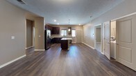 This single-floor residence is designed with a contemporary open-concept layout that seamlessly connects the kitchen, dining, and living areas. The living room is generously proportioned, featuring rich dark hardwood-style flooring, neutral taupe walls, white baseboards, a textured ceiling, and a sleek built-in electric fireplace that serves as a focal point. Pendant lighting adds a warm, modern touch throughout the space.

The kitchen is well-appointed and functional, showcasing rich dark espresso cabinetry that extends to the ceiling for ample storage, light granite countertops, and a large central island with additional seating potential. Stainless steel appliances, including a refrigerator with ice dispenser, range, microwave, and dishwasher, complete the kitchen.

The bedrooms feature plush carpeting, ceiling fans, and windows that invite natural light. The primary bathroom includes a dark espresso vanity with granite countertops, a walk-in shower, and direct access to a spacious walk-in closet with built-in wire shelving. A secondary bathroom offers a full tub-shower combination and a matching granite-topped vanity. The consistent use of dark cabinetry, granite surfaces, and hardwood-style flooring throughout creates a cohesive and polished aesthetic.