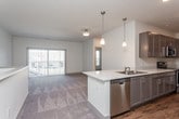 This single-story residence presents a thoughtfully designed open-concept layout that connects the main living areas with practical flow. The kitchen is a standout feature, outfitted with dark espresso cabinetry, granite-look countertops, and a full suite of stainless steel appliances, including a refrigerator, range, and microwave. Warm-toned hardwood-style flooring runs throughout the kitchen, grounding the space with a natural, durable finish. A peninsula counter provides additional workspace and serves as a natural division between the kitchen and the adjoining living area.

The living spaces are finished with plush, neutral-toned carpet that extends through the main gathering room and bedrooms, contributing to a comfortable and cohesive aesthetic. The bedroom offers a ceiling fan, a large window with exterior views, and ample wall space, creating a bright and airy retreat. A half-wall feature in the living area adds architectural interest while maintaining an open feel.

The bathroom is cleanly finished with matching dark cabinetry, granite-look countertops, a tub-shower combination, and hardwood-style flooring that ties back to the kitchen. Throughout the unit, neutral wall tones and consistent finishes create a unified, well-maintained interior.