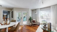 This single-floor residence offers a thoughtfully designed layout that balances comfort and functionality throughout its well-appointed rooms. The living area is a standout, featuring rich hardwood flooring, a textured ceiling, and an abundance of natural light streaming through large windows dressed with sheer white curtains. A set of classic French doors with multi-pane glass panels opens directly to an outdoor patio area, providing seamless indoor-outdoor connectivity and views of lush greenery.

The kitchen is equipped with white cabinetry, stone-look countertops, a mosaic tile backsplash, and stainless steel appliances. A pass-through counter connects the kitchen to the dining area, enhancing the open flow of the space.

The primary bedroom features plush carpet flooring, a stylish accent wall with a vertical striped wallcovering, and a walk-in closet. Additional bedrooms are equally well-finished — one showcasing a whitewashed shiplap accent wall and another with direct sliding door access to the outdoors. Both full bathrooms include tub-shower combinations, granite-style vanity countertops, white cabinetry, and warm hardwood-style flooring, maintaining a cohesive aesthetic throughout the home.