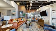 This generously sized 1-bedroom, 1-bathroom residence offers an impressive blend of industrial-chic and contemporary design across a single floor. The living area immediately captures attention with its dramatic exposed ceiling featuring steel beams, ductwork, and track lighting, complemented by striking exposed brick accent walls that lend warmth and character to the space. Large glass panels and tall windows allow abundant natural light to flow throughout, creating an open and inviting atmosphere.

The kitchen is well-appointed with rich dark wood cabinetry, gleaming granite countertops, a classic subway tile backsplash, and stainless steel appliances. A curved breakfast bar with seating provides a casual dining option and connects the kitchen seamlessly to the main living area, finished with durable wood-style flooring.

The bedroom offers a comfortable retreat, highlighted by a textured stone accent wall, ceiling fan, and plush carpeting underfoot. An adjoining walk-in closet features wire shelving, providing practical and organized storage. The bathroom includes a full tub-shower combination with white tile surround, wood-style flooring, and a vanity with granite countertops.

A hallway connects the rooms, completing a well-designed layout that balances urban industrial aesthetics with comfortable, functional living.