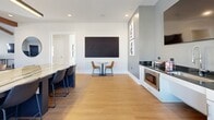 Located in Columbia, TN, this thoughtfully designed single-floor amenity space offers a generous, open layout that seamlessly blends recreation, work, and social gathering. Warm hardwood-style flooring runs throughout, complementing the crisp white walls and modern finishes that define the interior aesthetic.

The main open area is anchored by soaring vaulted ceilings adorned with rich, exposed wooden beams that add architectural character and a sense of volume to the space. Natural light pours in through multiple large windows, enhancing the bright and welcoming atmosphere. A full-size pool table and additional game tables serve as focal points for recreation, while ample open floor space allows for flexible use.

A well-appointed kitchenette features dark granite countertops, white cabinetry, a stainless steel sink with a professional-style faucet, a built-in microwave, and a large-format display mounted on a bold gray accent wall. A marble-topped island with bar seating and a cozy bistro table with leather chairs provide options for casual dining or conversation.

A dedicated workstation area lines one wall, equipped with desks, seating, and a wall-mounted flat-screen TV, making it ideal for productivity. Framed artwork and curated décor add refined touches throughout. A glass-paneled door connects to an adjacent corridor, contributing to the space's open and accessible flow.
