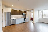Located at 2355 Franklin Ave E in Seattle's vibrant Capitol Hill neighborhood, this well-appointed one-bedroom, one-bathroom residence offers a thoughtfully designed layout with modern finishes throughout. Hardwood-style flooring runs continuously through all areas, lending warmth and visual cohesion to the space.

The open-concept kitchen is a standout feature, showcasing two-tone cabinetry with rich dark wood upper cabinets and light lower cabinets, a white tile backsplash, white quartz countertops, and a full suite of stainless steel appliances including a gas range, microwave, dishwasher, and refrigerator. A sliding door off the kitchen leads to a private balcony, allowing natural light to flow into the living area.

A clean, well-lit hallway connects the living spaces to the bedroom and bathroom. The bedroom features large corner windows that flood the room with natural light and offer views of the surrounding neighborhood, complemented by a sliding-door closet for ample storage. The bathroom includes a wide vanity with white cabinetry, a tub-shower combination, and a large mirror. Conveniently tucked near the kitchen, an in-unit stacked washer and dryer adds everyday practicality to this streamlined urban residence.