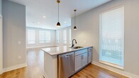 Located at 199 Dickenson Street in Columbus, OH, this well-appointed one-bedroom, one-bathroom unit offers a thoughtfully designed layout across a single floor. The open-concept kitchen and living area serves as the heart of the home, featuring warm hardwood-style flooring, recessed lighting, and multiple windows dressed with white blinds that invite generous natural light. The kitchen is a standout, centered around a granite-topped island with an undermount sink and elegant brass pendant lights overhead. Crisp grey cabinetry, a tile backsplash, and a full suite of stainless steel appliances—including a refrigerator, range, microwave, and dishwasher—complete the space. The living area extends seamlessly from the kitchen, offering a bright and open atmosphere with a row of windows along the exterior wall. The bedroom provides a comfortable retreat with plush carpeting, soft grey walls, and a natural light-filled window. A dedicated closet adds practical storage. The bathroom is finished with large-format marble-look tile flooring, a grey vanity with granite countertop, a framed mirror, and a soaking tub/shower combination—all accented with sleek matte black hardware for a contemporary touch.