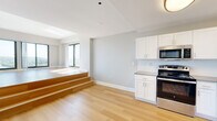 This thoughtfully designed one-bedroom, one-bathroom residence at 170 Washington Street in Haverhill, MA offers a bright and modern living experience with an open, airy layout throughout. Light hardwood flooring flows seamlessly across the entire unit, complementing the neutral gray-toned walls and crisp white trim that give the space a clean, contemporary feel.

The combined kitchen and living area is a standout feature, highlighted by a striking split-level design with wooden steps leading up to an elevated living space. Floor-to-ceiling windows and sliding glass doors flood the area with natural light and frame breathtaking panoramic views of the waterfront and surrounding landscape. A private balcony extends the living space outdoors, perfect for enjoying the scenery.

The kitchen is well-appointed with white shaker-style cabinetry, a white tile backsplash, gray countertops, and a full suite of stainless steel appliances, including a refrigerator, range, microwave, and dishwasher.

The spacious primary bedroom offers generous proportions and includes access to a dedicated walk-in closet, providing ample storage. The bathroom features a clean, functional design with a combined tub and shower, a white vanity, and hardwood-style flooring. A hallway closet provides additional storage, completing this well-appointed residence.