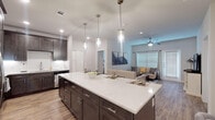 This single-story residence showcases a thoughtfully designed open-concept layout that seamlessly connects the kitchen, dining, and living areas. The kitchen is a standout feature, anchored by a generously sized island with a bright white quartz countertop and seating for multiple guests. Dark espresso-toned shaker cabinets extend to the ceiling, providing ample storage, while stainless steel appliances, a subway tile backsplash, and three pendant lights overhead complete the contemporary look. Wood-look plank flooring flows consistently throughout the main living areas, adding warmth and cohesion.

The living room is comfortable and well-lit, benefiting from natural light through large windows dressed with blinds and curtains. A ceiling fan adds both function and style, while a glass door provides additional access and light.

Two bedrooms each offer ceiling fans, natural light from windows, and a calm, neutral palette. The primary bathroom features a dual-sink vanity with a backlit mirror, a glass-enclosed walk-in shower, and tile flooring. The secondary bathroom includes a full tub-shower combination with white cabinetry and tile flooring. Together, the rooms present a cohesive, modern aesthetic suited for everyday living.