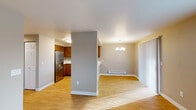 This single-floor residence offers a practical and well-organized layout designed for comfortable everyday living. The open-concept main area seamlessly connects the kitchen and living/dining spaces, divided by a partial wall that adds architectural definition without sacrificing openness. The kitchen is equipped with warm-toned wood cabinetry, white countertops, a stainless steel refrigerator, and a stainless electric range with an overhead exhaust hood. A peninsula with a built-in sink provides additional prep space and overlooks the adjoining areas. Hardwood-style flooring runs throughout the main living areas, while a chandelier adds a refined touch to the dining space. Natural light filters in through large windows fitted with horizontal blinds and vertical panel blinds near the sliding door, which opens to outdoor views of surrounding trees. The two bedrooms feature plush carpeting, neutral-toned walls, and windows that bring in natural light. The bathroom is well-appointed with a wood-finish vanity, white countertop, and a shower/tub combination, with the added convenience of an in-unit washer and dryer. Baseboard heaters are present throughout, and the overall palette of warm neutrals and natural wood tones creates a cohesive, understated ambiance.