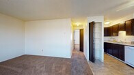 This single-floor unit offers a practical and well-organized layout designed for comfortable everyday living. The open living area is finished with plush wall-to-wall carpeting and neutral-toned walls, creating a clean and versatile canvas. A ceiling fan overhead and a baseboard heating system ensure year-round comfort. A large window allows natural light to fill the space, enhancing the bright and airy feel throughout.

The kitchen is efficiently designed with dark espresso cabinetry extending from floor to ceiling, providing generous storage. It is equipped with a range, a refrigerator, and a dishwasher, all set against tile flooring and light countertops. An adjacent built-in shelving unit adds additional storage and organizational convenience just off the kitchen.

The bedroom is a well-proportioned, carpeted room with a window dressed with blinds, a baseboard heater, and ample wall space. The textured ceiling is consistent throughout the unit, adding a subtle architectural detail.

The bathroom features a full-size soaking tub and shower combination with clean white surrounds and chrome fixtures, accessed through a dark-toned door. A hallway connects the main living spaces and includes a built-in open shelving unit, ideal for storage or display. Overall, the unit presents a functional, clean, and comfortable living environment.
