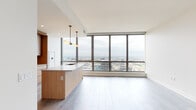 Located in Chicago's vibrant West Loop neighborhood, this single-floor high-rise residence at 164 N Peoria St offers a refined contemporary living experience defined by clean lines and upscale finishes. The open-concept living and kitchen area is the centerpiece of the unit, anchored by dramatic floor-to-ceiling windows that frame expansive panoramic views of the Chicago skyline and cityscape, flooding the space with natural light. Light-toned wood-style flooring runs throughout, enhancing the bright, airy atmosphere.

The kitchen is thoughtfully designed with a large waterfall-edge island topped in quartz, a stainless steel sink, and a gas range with a built-in range hood. Custom flat-panel cabinetry in warm wood tones is complemented by a textured tile backsplash, while sleek cylindrical pendant lights add a modern, sculptural touch overhead.

The bedrooms are well-proportioned with neutral walls and generous closet access, maintaining the clean, minimalist aesthetic of the home. A secondary room provides flexible space suited for a bedroom or office.

The bathrooms reflect the same high standard of design: one features a floating wood-toned vanity with a dual-sink white countertop, a large framed mirror, and tile flooring, while the second bath offers an open metal-framed vanity with a concrete-finish countertop and a bold circular mirror, delivering a modern, industrial-chic contrast.