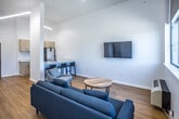 This single-floor unit in Jonesboro, Arkansas, offers a thoughtfully designed layout that maximizes functionality within a compact footprint. The open-concept living area is characterized by soaring ceilings and crisp white walls that enhance the sense of space. Large windows fitted with roller shades flood the room with natural light while framing views of the surrounding cityscape, and a glass door provides direct access to a private balcony. Light-toned hardwood-style flooring runs throughout, lending warmth and continuity to the interior.

The galley-style kitchen features light wood cabinetry with clean-lined hardware, white quartz countertops, and stainless steel appliances, including a range, microwave, refrigerator, and dishwasher. The layout is efficient, with ample counter space on both sides of the walkway.

The full bathroom includes a shower-tub combination with a sleek glass panel and brushed hardware accents, complemented by natural wood-toned door details. A separate half bath offers a white vanity with cabinet storage, a wall mirror with overhead lighting, and matching hardwood-style flooring, providing added convenience for guests. Together, the spaces present a clean, modern aesthetic suited for comfortable everyday living.