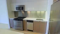 This two-floor space showcases a modern, minimalist aesthetic with clean lines and contemporary finishes. The kitchen is a standout feature, equipped with a full suite of stainless steel appliances, including a gas range, over-the-range microwave, and dishwasher. A stainless steel backsplash adds an industrial touch, while the light wood lower cabinetry contrasts neatly with the crisp white upper cabinets, creating a balanced, two-tone design. Light-colored countertops provide ample workspace, and an undermount stainless steel sink completes the functional layout. Recessed under-cabinet lighting illuminates the countertops effectively. The cabinetry features sleek, handleless or minimalist hardware, reinforcing the contemporary style. Light-toned tile flooring runs through the kitchen, contributing to an open, airy feel. The overall design of the space prioritizes clean, functional aesthetics, with a cohesive material palette that ties together modern and practical elements across both floors.