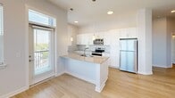 Located on North Meridian Street in Indianapolis, this thoughtfully designed 2-bedroom, 3-bathroom residence offers a clean, modern aesthetic throughout its single-floor layout. Light hardwood-style flooring flows through the main living areas, complementing the bright white walls and recessed lighting that give the space an open, airy feel.

The combined kitchen and living area serves as the heart of the home. The kitchen features white shaker cabinetry extending to the ceiling, stainless steel appliances including a refrigerator, range, and microwave, and a central island with a built-in sink and pendant lighting overhead. Large windows and a glass door invite abundant natural light and provide views of the surrounding Indianapolis skyline.

A central hallway connects the living area to the two bedrooms, each carpeted for comfort and fitted with ceiling fans. The primary bedroom is generously sized and includes a walk-in closet with wire shelving systems offering ample storage. Both bedrooms benefit from large windows with expansive city views.

The three bathrooms are finished with wood-look tile flooring, white cabinetry with framed mirrors, and neutral countertops. One bathroom includes a tub-shower combination with tile surround. Additional conveniences include a dedicated laundry area and a utility room, rounding out a well-appointed, functional living space.