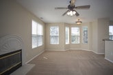 This single-floor home offers a comfortable and functional layout designed for everyday living. The main living area is generously proportioned, featuring warm beige carpet, a ceiling fan with light fixture, and a decorative arched fireplace flanked by windows that invite ample natural light. An adjacent area opens to a private balcony through sliding glass doors, extending the living space outdoors with views of surrounding greenery.

The open-concept layout connects the living area to a dining space and kitchen, which is outfitted with warm honey-toned wood cabinetry, dark granite-style countertops, tile flooring, and a full suite of black appliances including a range, over-the-range microwave, refrigerator, and dishwasher. A built-in desk area with matching cabinetry provides a convenient workspace just off the main living zone.

The bedrooms are carpeted and generously sized, each featuring walk-in closets with built-in shelving for organized storage and windows providing natural light. Two full bathrooms serve the home, both finished with patterned tile flooring, white vanities with dark countertops, and a tub-shower combination. The overall aesthetic throughout is neutral and clean, with warm beige tones creating a cohesive and inviting atmosphere.