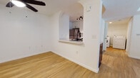 This single-floor residence offers a thoughtfully designed open layout highlighted by warm hardwood-style flooring that flows consistently throughout every room. The living area is bright and airy, featuring a ceiling fan and French doors fitted with blinds that allow natural light to pour in while providing privacy. An elegant arched pass-through connects the living space to the kitchen, creating a sense of openness while maintaining a defined separation between the two areas. The kitchen is well-appointed with stainless steel appliances, including a refrigerator, range, and over-the-range microwave, complemented by white cabinetry, a geometric tile backsplash, and clean white countertops. A matte black gooseneck faucet serves as a stylish focal point at the sink. Adjacent to the kitchen, an in-unit washer is conveniently accessible. The bedroom features neutral white walls, a ceiling fan with light fixture, and a window with blinds that brings in soft natural light. The bathroom includes a white vanity with dark hardware, a round black-framed mirror, and a full soaking tub with shower. Throughout the space, bright white walls and clean baseboards contribute to a crisp, modern, and move-in-ready aesthetic.