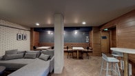 Located at 624 Yale Avenue North in Seattle's South Lake Union neighborhood, this single-floor lounge space offers a thoughtfully designed interior that blends industrial and contemporary aesthetics. The herringbone-patterned wood flooring runs throughout, providing a warm foundation that contrasts beautifully with the dark ceiling and exposed concrete structural column at the room's center.

The space is divided into distinct seating zones. A tufted leather banquette lines the far wall, set against a deep navy penny-tile accent wall marked with the building's address, "624," and paired with white marble-top tables and black dining chairs—ideal for social gatherings. A separate lounge area features a plush sectional sofa, a wingback plaid accent chair, and a low round coffee table arranged in front of a large wall-mounted flat-screen television, all anchored by a white brick feature wall adorned with hanging framed artwork.

Near the entry, warm wood-paneled walls frame a natural wood door, accompanied by a high-top bistro table with stools—a perfect spot for casual conversation. A built-in wet bar with white countertops, under-counter storage, and subway tile backsplash provides convenient beverage service. Recessed and pendant lighting throughout creates a warm, inviting ambiance suited for both relaxed lounging and communal entertaining.