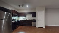 This single-floor residence showcases a thoughtfully designed open-concept layout, where the kitchen and living area flow seamlessly together. The kitchen is a standout feature, outfitted with rich dark espresso cabinetry, granite countertops, and a neutral-toned tile backsplash. A full suite of stainless steel appliances — including a refrigerator, range, microwave, and dishwasher — adds a modern, polished finish. Track lighting overhead enhances both functionality and ambiance in the cooking space.

Warm wood-style flooring runs throughout the unit, lending a cohesive and inviting feel to every room. The open living area benefits from a ceiling fan and is anchored by French doors that lead to a private balcony, bringing in natural light and outdoor views.

A dedicated laundry area houses a full-sized washer and dryer alongside wire shelving for added storage convenience. The bathroom features dark vanity cabinetry with contrasting light countertops, continuing the design language found in the kitchen. Neutral gray walls throughout the unit create a calm, versatile backdrop, while clean white trim and doors provide a crisp, finished aesthetic.