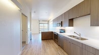 This contemporary studio in Denver's 80211 zip code offers a thoughtfully designed open-concept layout that maximizes every square foot. Light wood-tone flooring runs throughout, creating a warm and cohesive aesthetic that ties all areas of the space together seamlessly.

The kitchen is a standout feature, outfitted with rich dark wood cabinetry extending to the ceiling for ample storage, white quartz countertops, and a full suite of stainless steel appliances including a range, microwave, dishwasher, and refrigerator. A large garage-style window at the far end of the living area draws in generous natural light and adds an industrial-modern character to the space.

The living area is open and airy, enhanced by a ceiling fan and clean white walls that lend a bright, versatile canvas. A dedicated closet with built-in shelving provides practical storage. The bathroom features large-format tile flooring, a tub-shower combo with classic white subway tile surround, a wood-paneled vanity with an undermount sink, and a frameless mirror. A separate laundry area adds everyday convenience. This studio offers a well-appointed, efficient living experience in a modern Denver setting.