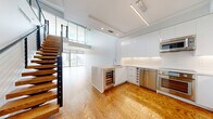 This two-story residence in Dallas, TX offers a generous and thoughtfully designed layout spread across two floors. Rich hardwood flooring flows throughout, complemented by crisp white walls and abundant natural light. The entry level features a welcoming foyer with built-in shelving and a striking open-tread staircase with a sleek metal frame, serving as an architectural focal point that connects both levels. The modern kitchen is outfitted with high-gloss white cabinetry, stainless steel appliances, a built-in wine cooler, and a peninsula, opening seamlessly to the combined dining and living area. Floor-to-ceiling glass walls and sliding doors reveal panoramic Dallas skyline views and lead to a spacious wraparound balcony enclosed by glass railings. The upper level houses the primary bedroom, which benefits from expansive city views through large floor-to-ceiling windows. The bathroom features large-format tile flooring, a soaking tub with stone-look tile surround, and a clean, minimalist vanity. A dedicated office, two well-appointed closets with adjustable shelving systems, and an in-unit laundry room with full-size Whirlpool washer and dryer complete this residence's practical offerings.