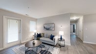 This single-floor residential unit offers a well-organized layout designed for comfortable everyday living. The main living area is a standout feature, boasting a distinctive tray ceiling that adds architectural depth and a sense of elevated space. Neutral-toned walls and soft wall-to-wall carpeting throughout the living and bedroom areas create a cohesive, move-in-ready aesthetic. A programmable thermostat is conveniently located in the main living space.

The galley-style kitchen is efficiently designed with ample white cabinetry lining both sides, providing generous storage. It is equipped with black appliances, including an electric range, refrigerator, and dishwasher, along with a double-basin sink and light-toned countertops. Light tile flooring completes the functional workspace.

The bedrooms are comfortably sized with neutral carpeting and soft grey walls. One bedroom benefits from a window with blinds, allowing natural light to filter in. Panel-style interior doors add a clean, classic detail throughout.

A dedicated laundry area includes both electric and water hookups along with overhead wire shelving, offering added in-unit convenience. The bathroom is fitted with a full tub and shower combination, tile flooring, a vanity, and chrome fixtures, providing a clean and practical space.
